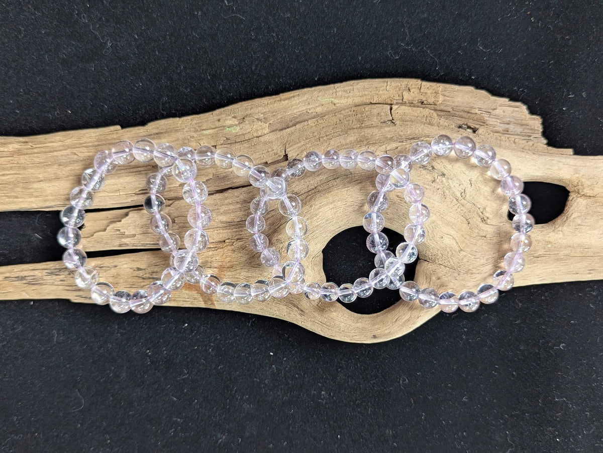 A full lineup of Light Amethyst bracelets from Bolivia ranging from 7mm to 10mm sizes, arranged sequentially on natural driftwood.