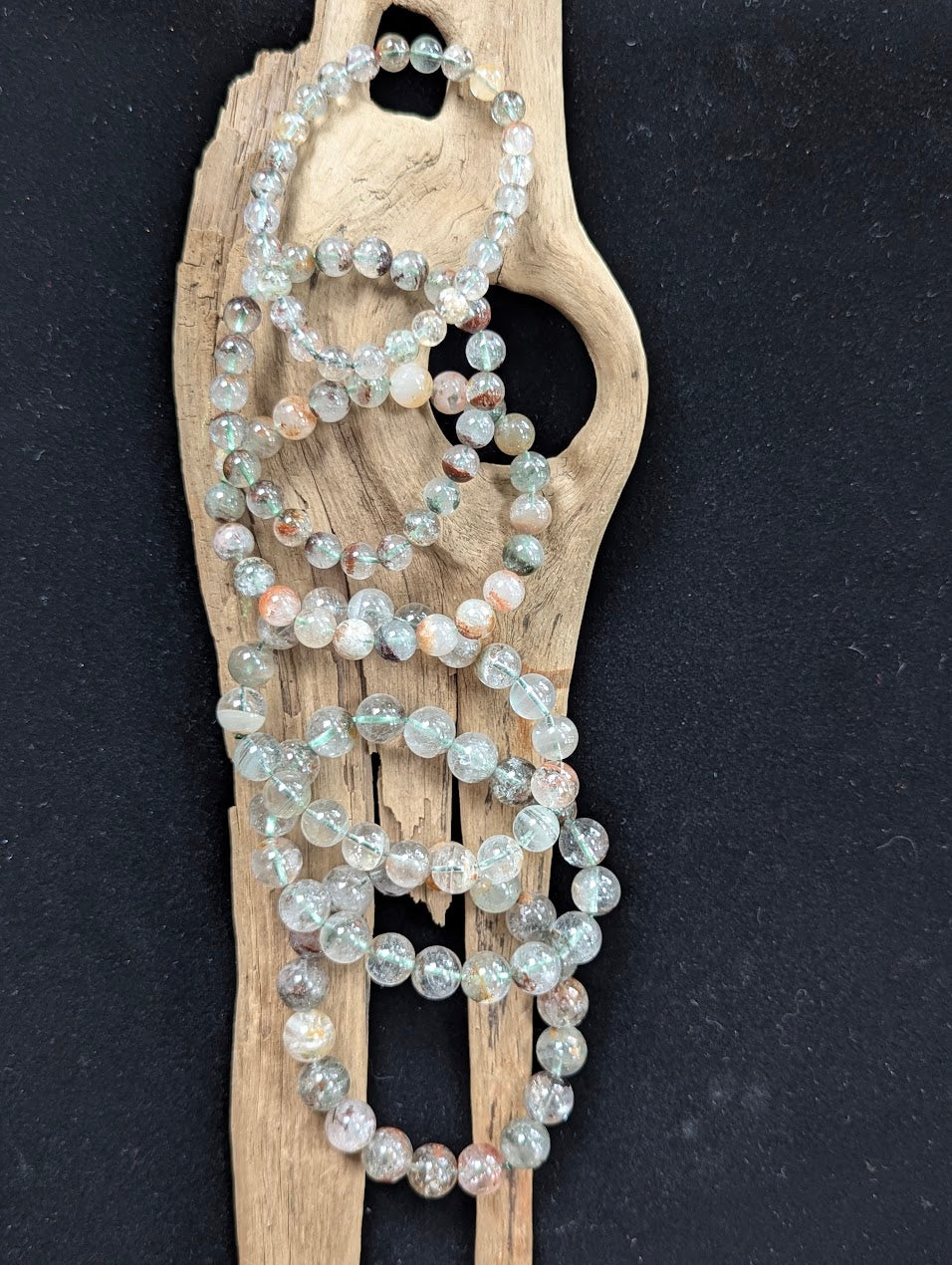 Assorted sizes of Light Garden Quartz (Lodolite) Bracelets arranged vertically on a piece of natural driftwood.