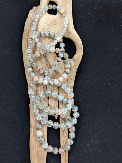 Assorted sizes of Light Garden Quartz (Lodolite) Bracelets arranged vertically on a piece of natural driftwood.