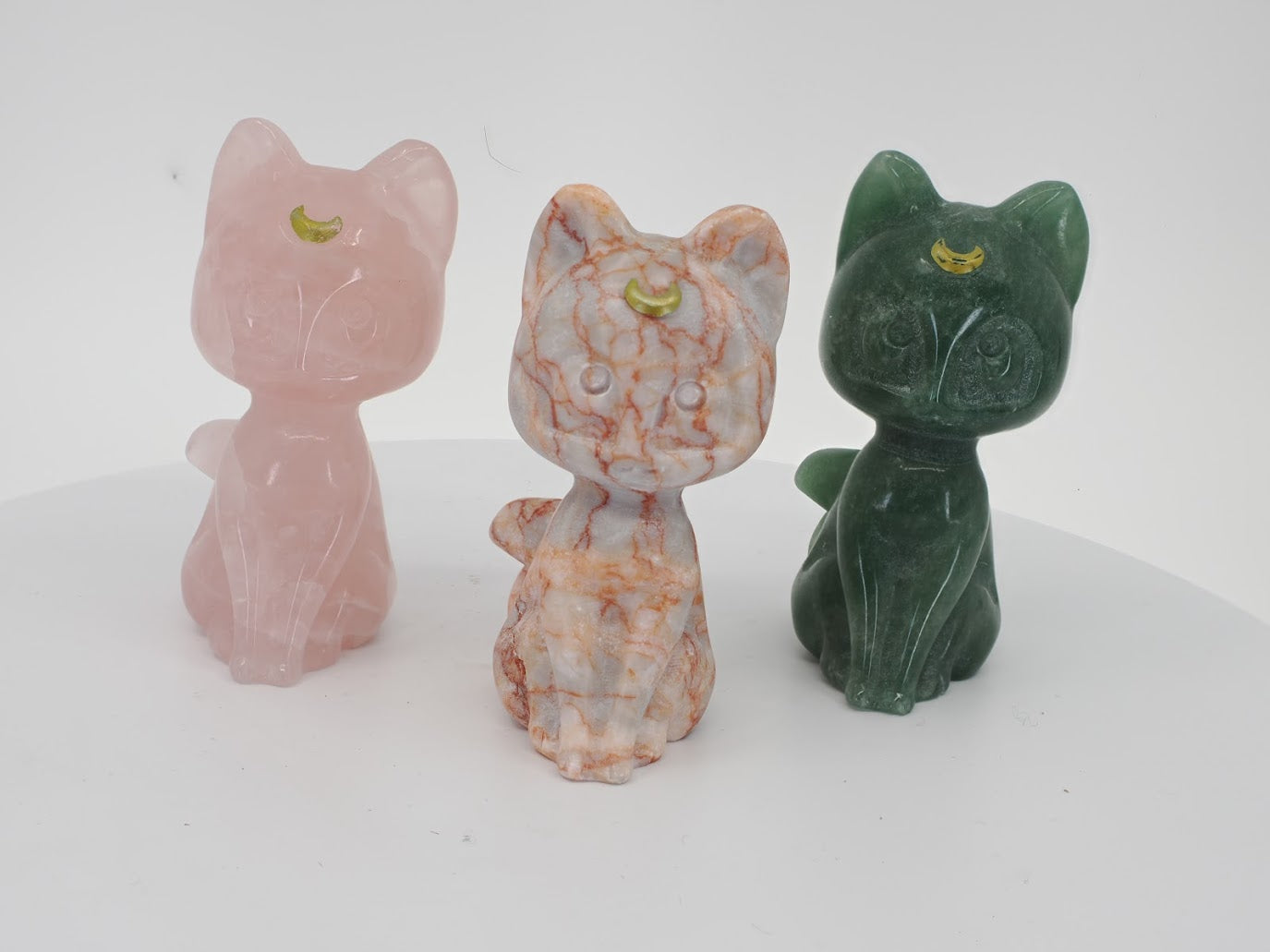 Three 3-inch hand-carved Luna cat figurines in Rose Quartz, Green Aventurine, and Red Vein Jasper with gilded moon details.