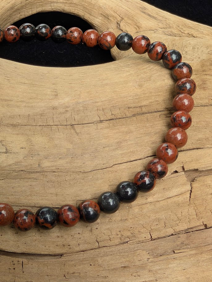 Macro close-up of 4mm polished Mahogany Obsidian beads highlighting the high-gloss finish and natural black and red volcanic glass patterns.