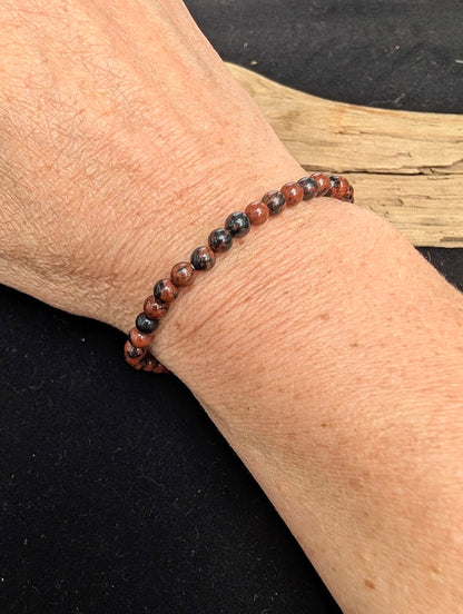 4mm polished Mahogany Obsidian beaded stretch bracelet worn on a wrist for delicate size scale.