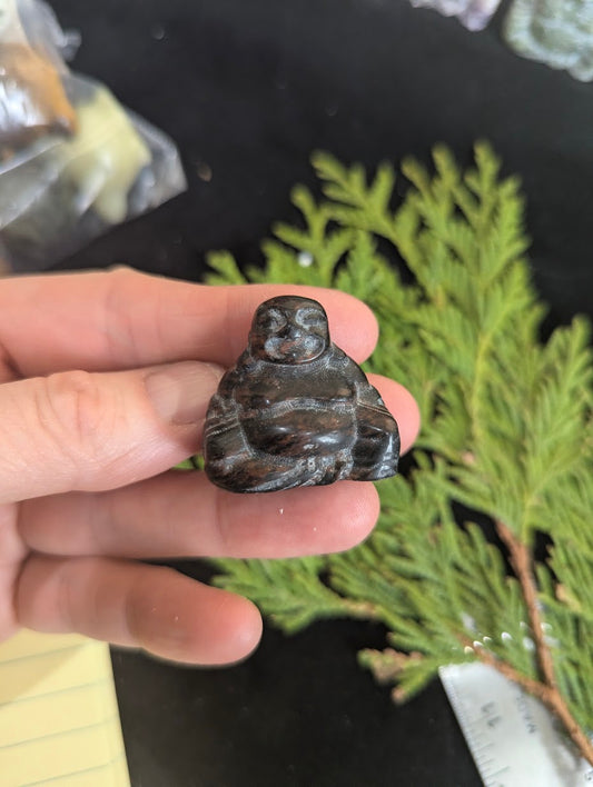 Handheld view of a 3cm Mahogany Obsidian Buddha totem showing dark black glass with reddish-brown iron inclusions and high-polish finish.
