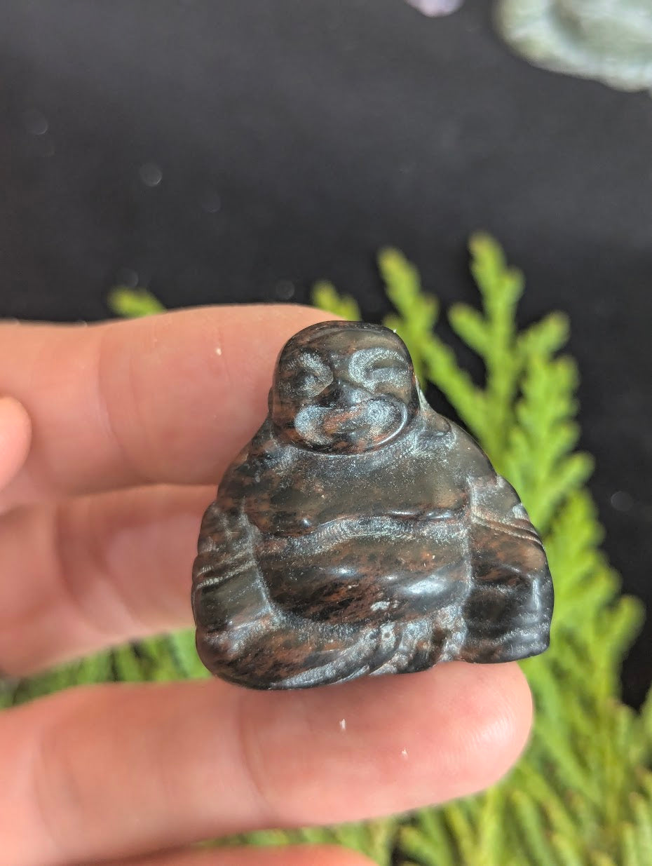 Macro photograph of a 3cm Mahogany Obsidian Buddha totem highlighting the natural volcanic glass texture and artisan carving details.