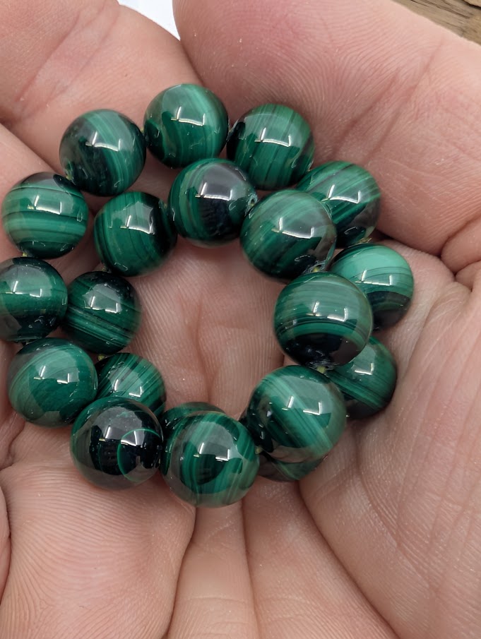 Handheld view of 10mm malachite bracelet showing deep green colour and bold natural banding