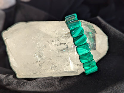 Natural banded malachite segmented bracelet displayed on a clear quartz specimen.
