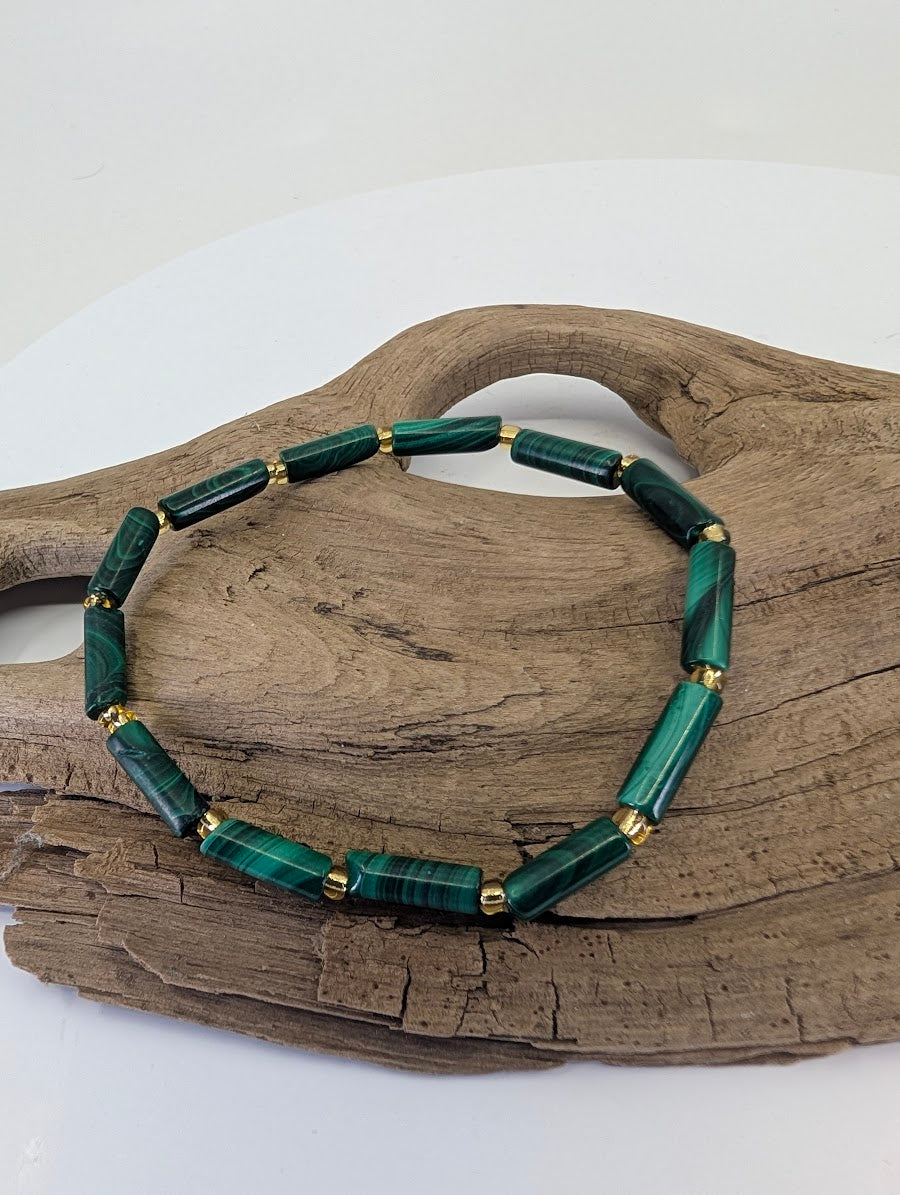 Congolese Malachite tube bead bracelet with gold spacers displayed on natural wood showing banded patterns.