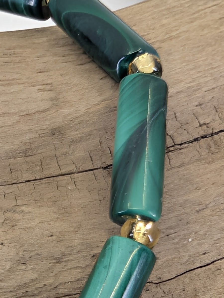 Macro view of a Malachite tube bead showing silky luster and intricate forest-green mineral growth layers.