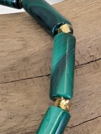 Macro view of a Malachite tube bead showing silky luster and intricate forest-green mineral growth layers.