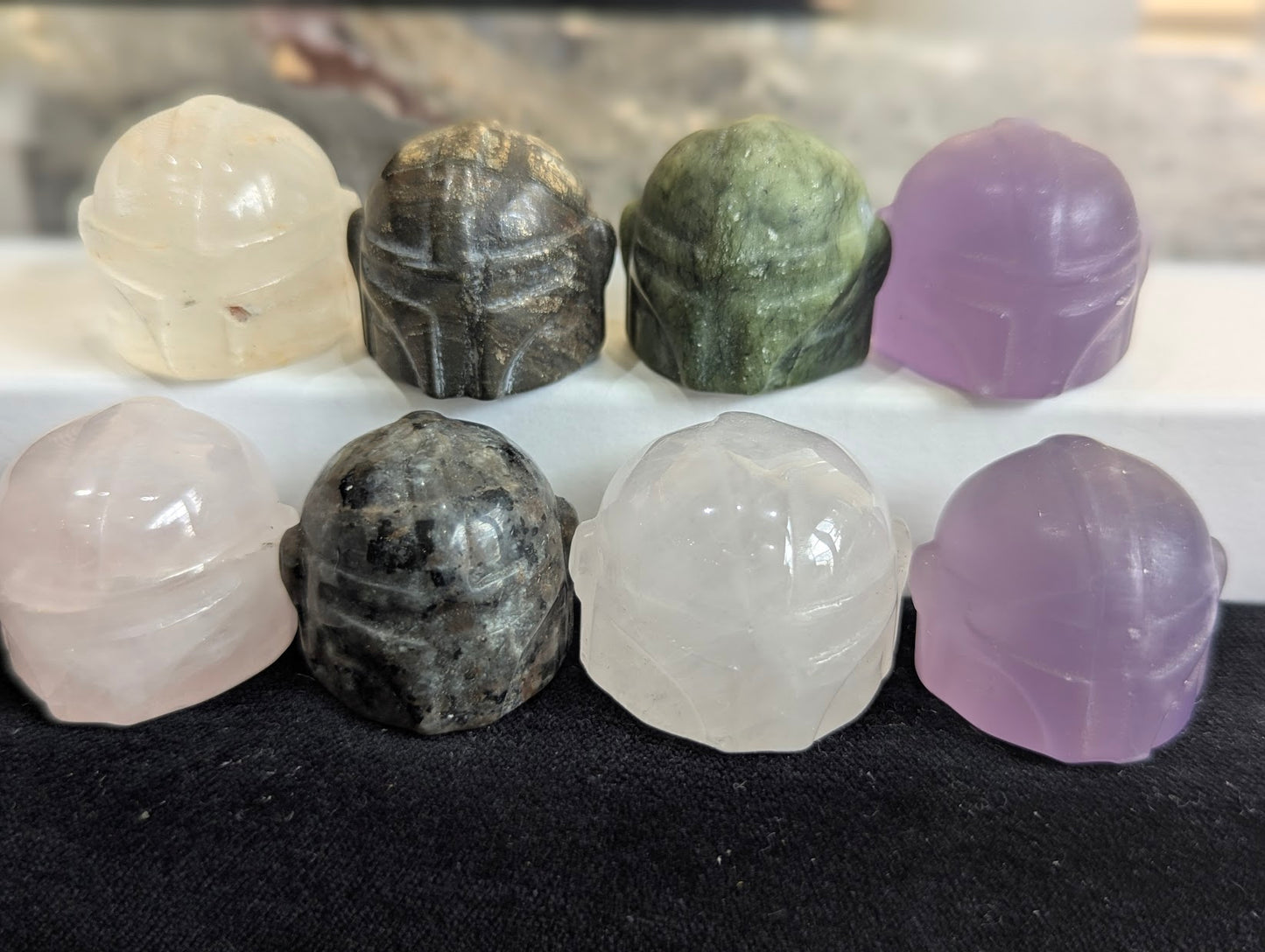 A group of eight precision-carved Mandalorian helmet totems in various natural minerals.