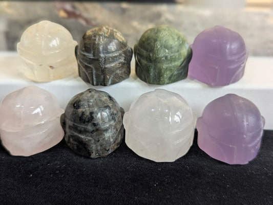 A group of eight precision-carved Mandalorian helmet totems in various natural minerals.