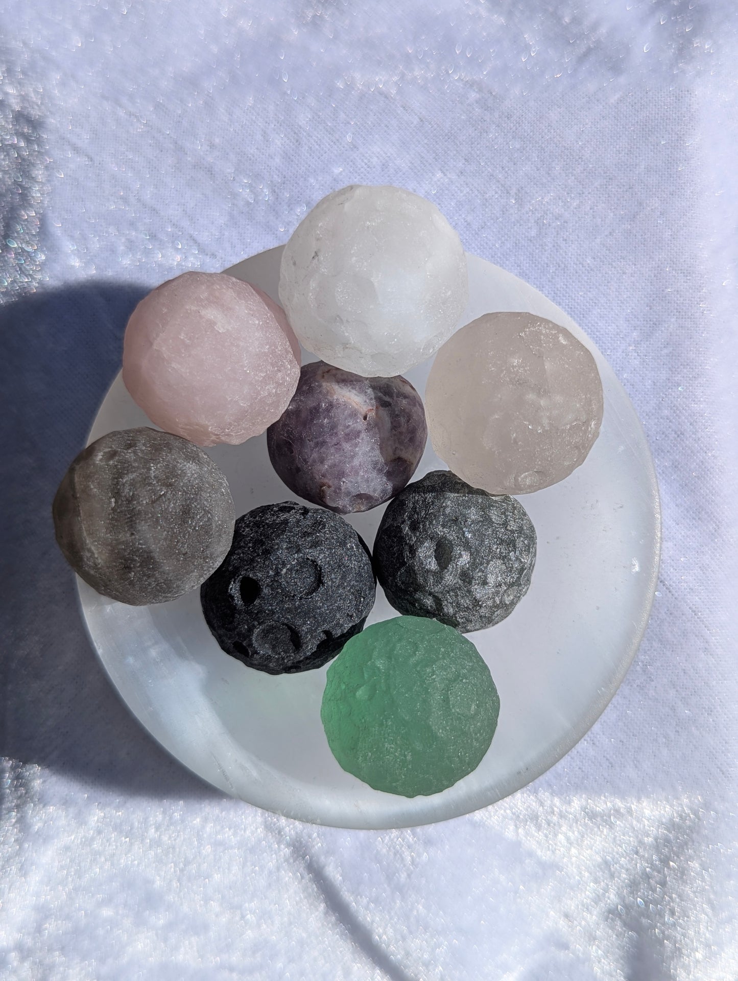 Multiple 30 mm (1.18 in) mini carved mineral moon spheres arranged in a white satin spar bowl against a white fabric background.