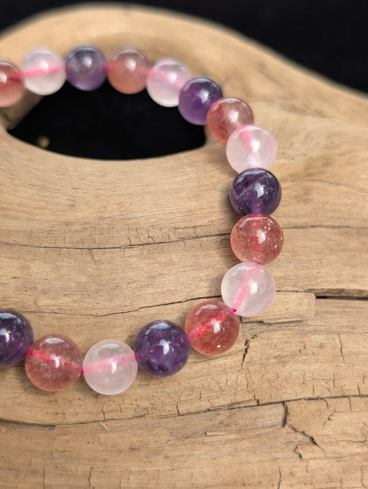 Macro view of polished 8mm mixed quartz spherical beads on driftwood, highlighting the natural red iron oxide inclusions within the Strawberry Quartz.