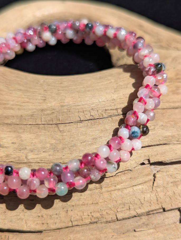 Macro close-up of hand-woven mixed Tourmaline highlighting the tiny polished micro-beads and the structure of the bright pink weaving cord.