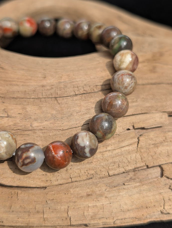 Macro view of polished 8mm Money Agate spherical beads on driftwood, highlighting the natural banding and complex earthy patterns.