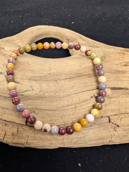 4mm polished Mookaite beaded stretch bracelet resting on a driftwood display, showing earthy burgundy, yellow, and cream tones.