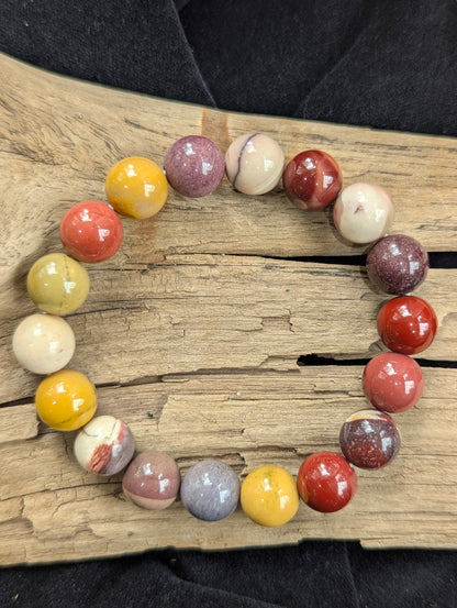 A 10mm Mookaite stretch bracelet displayed on driftwood, offering a vivid spectrum of natural, unaltered silicified chert colours.