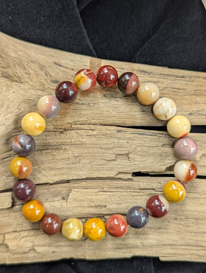 An 8mm Mookaite round bead stretch bracelet resting on natural driftwood, highlighting the smooth surface polish and rich earthy matrix colours.