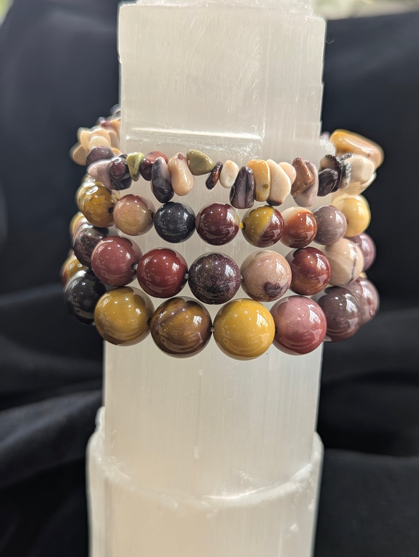 Authentic, un-stabilized Mookaite stretch bracelets from Western Australia resting on a white Selenite tower, showcasing vivid earthy burgundy and mustard matrix colours.