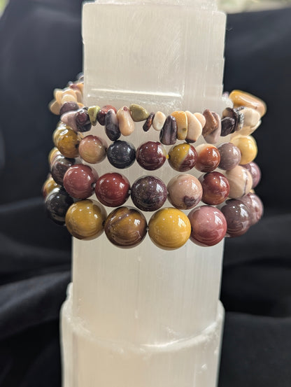 Authentic, un-stabilized Mookaite stretch bracelets from Western Australia resting on a white Selenite tower, showcasing vivid earthy burgundy and mustard matrix colours.