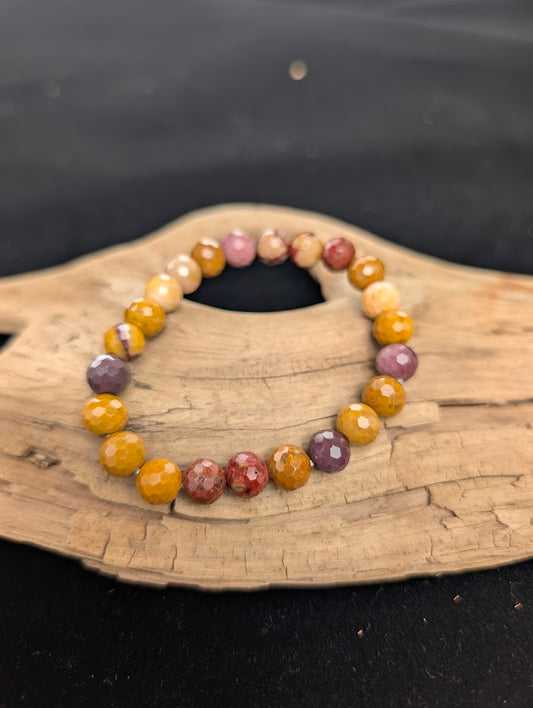 8mm faceted Mookaite beaded stretch bracelet resting on a driftwood display, showing vibrant earthy red and yellow colours.