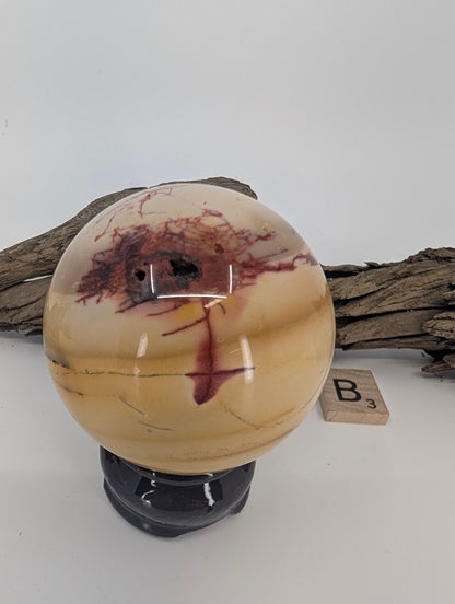 Creamy Mookaite sphere with red dendritic lightning veins and natural texture.