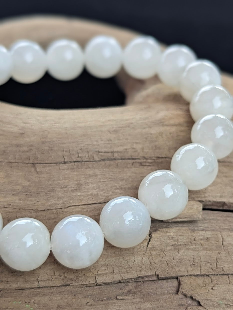 Close-up of a 10mm white Sri Lankan Moonstone bracelet showing natural blue adularescence on driftwood.