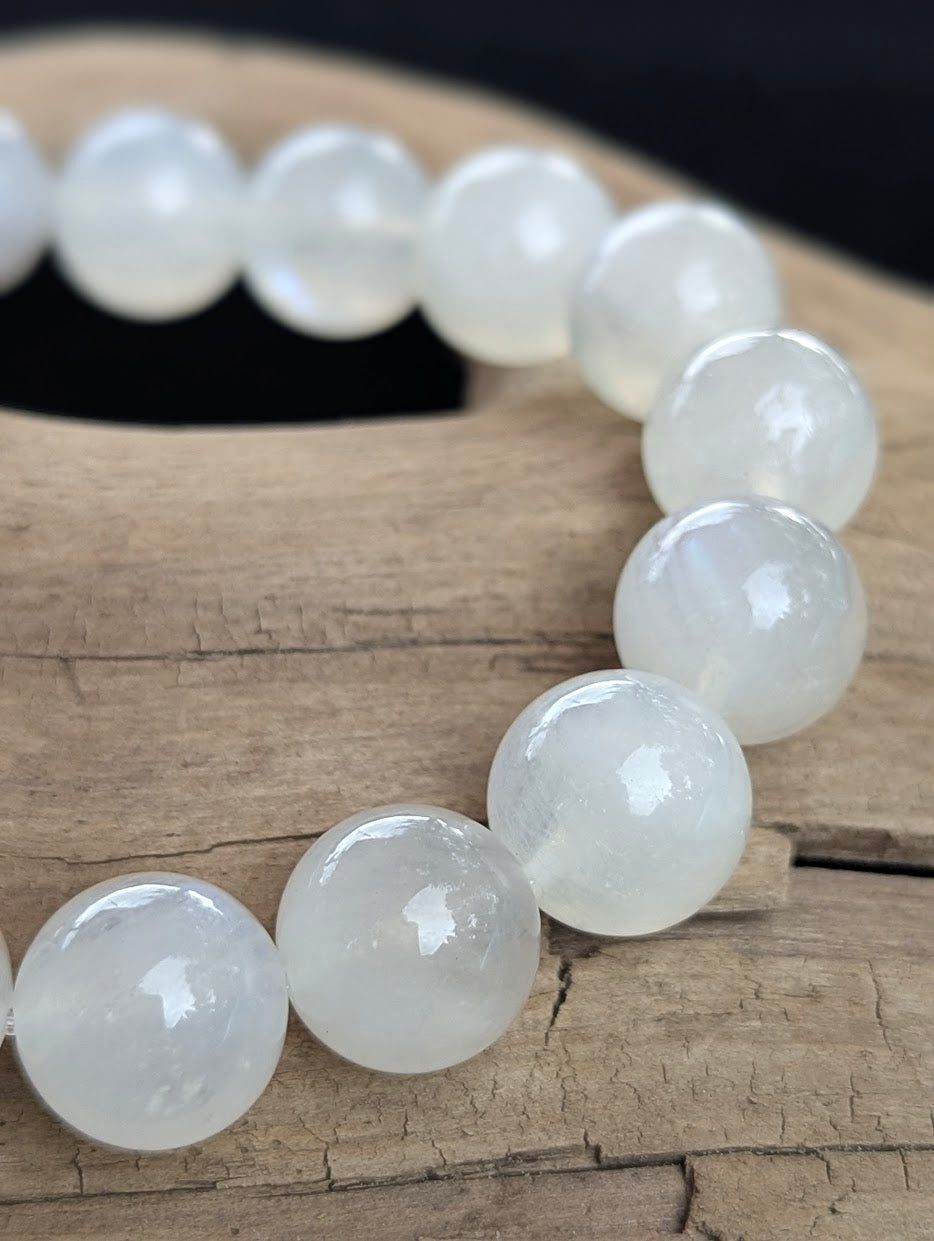 Close-up of a 12mm white Sri Lankan Moonstone bracelet displaying dynamic blue flash on the polished beads.