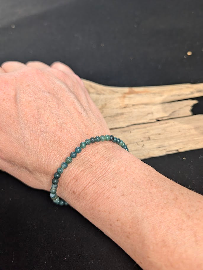 Natural sunlight on a 4mm earthy green Moss Agate stretch bracelet worn on a wrist.