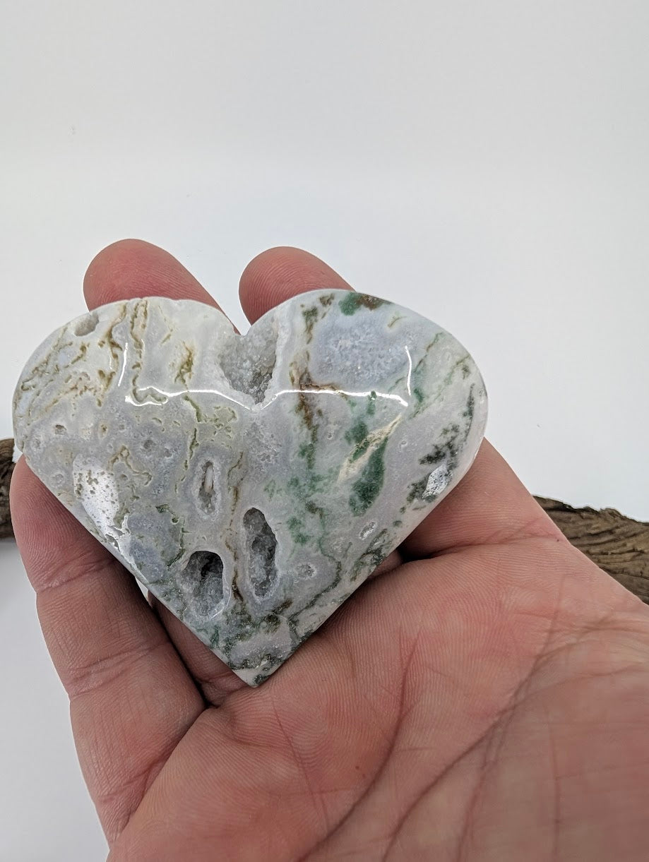 Hand holding Specimen A, a 130g Moss Agate heart with deep open crystal vug.