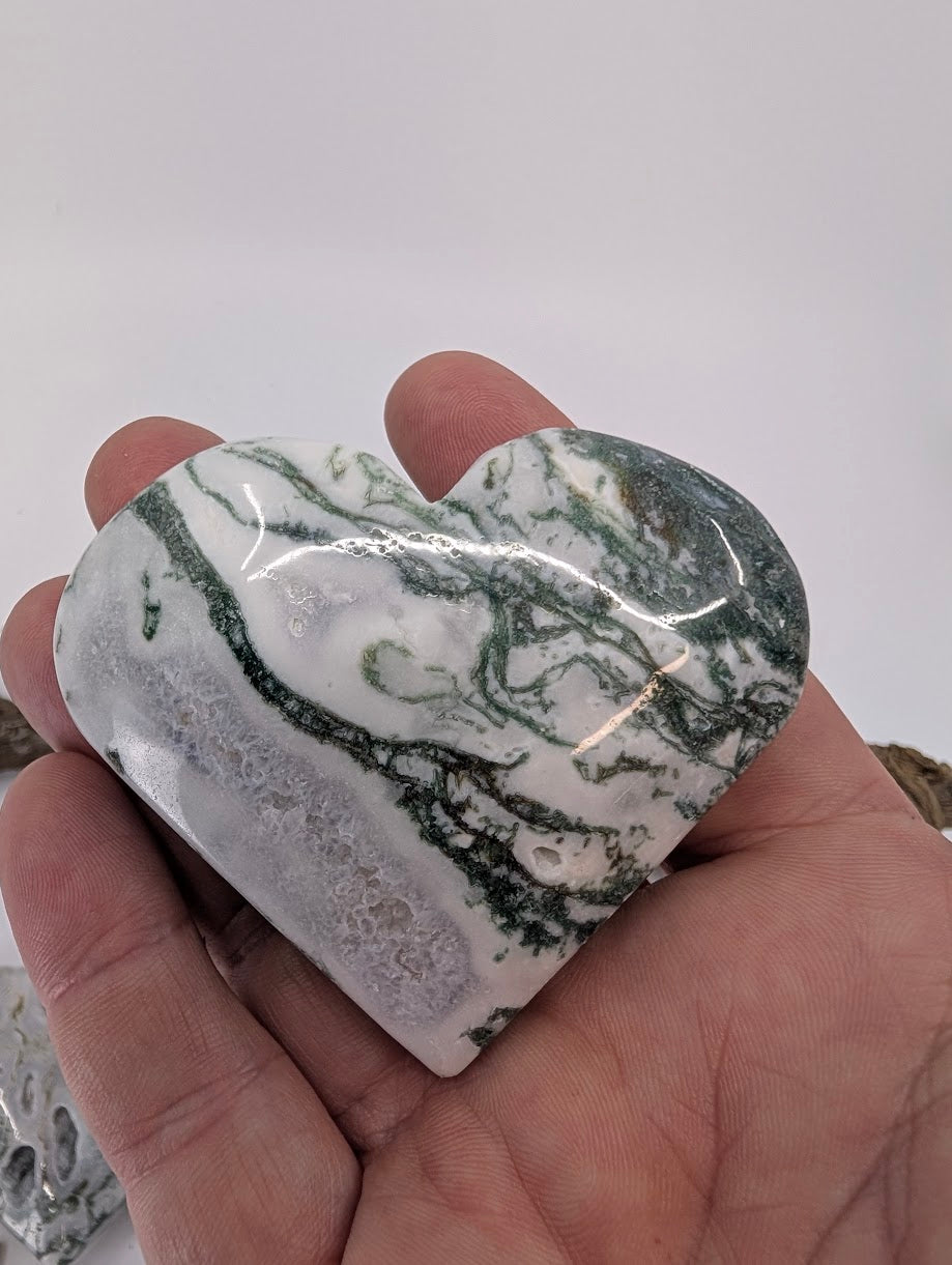 Hand holding Specimen B, a 140g Moss Agate heart with green moss patterns.
