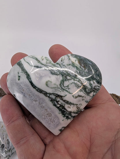 Hand holding Specimen B, a 140g Moss Agate heart with green moss patterns.
