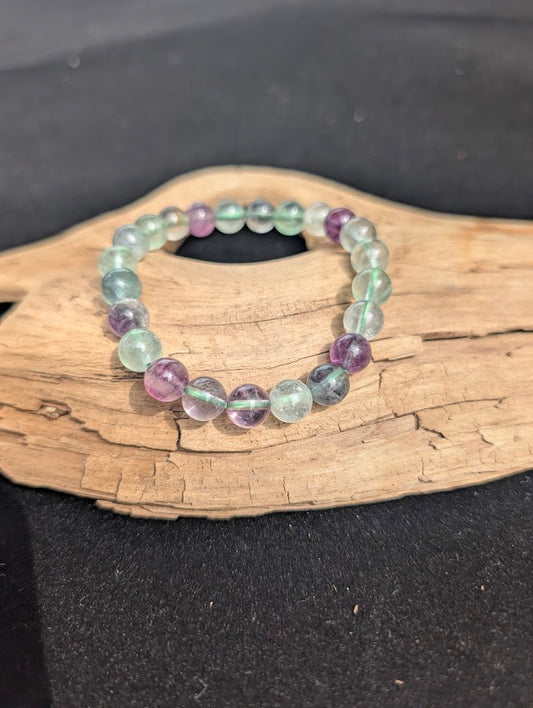 8mm multi-colour green and purple fluorite beaded bracelet resting on a driftwood display, showing green cord detail.