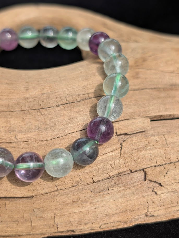 Macro close-up of 8mm translucent green and purple fluorite beads showing natural internal structures and a green stretch cord.