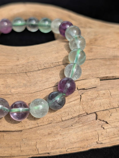 Macro close-up of 8mm translucent green and purple fluorite beads showing natural internal structures and a green stretch cord.