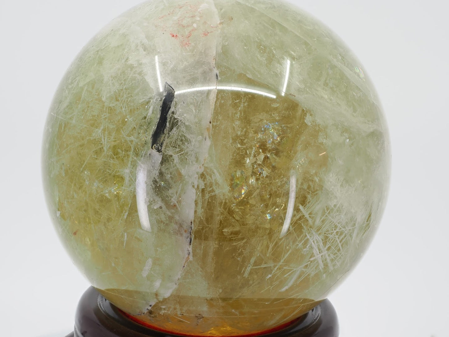 Zambian Citrine sphere featuring a distinct dark mineral rod inclusion and internal rainbow fractures.