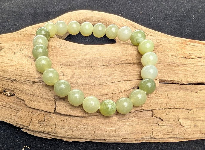 8mm polished New Jade Serpentine beaded stretch bracelet resting on a driftwood display, showing translucent pale celadon green tones.