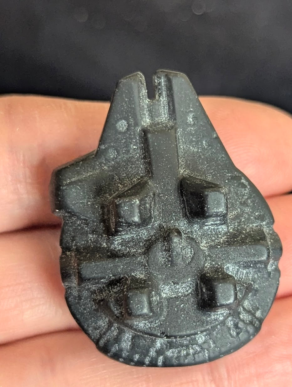 Underside view of a matte black obsidian Millennium Falcon carving showing the base structure and dark volcanic glass texture.
