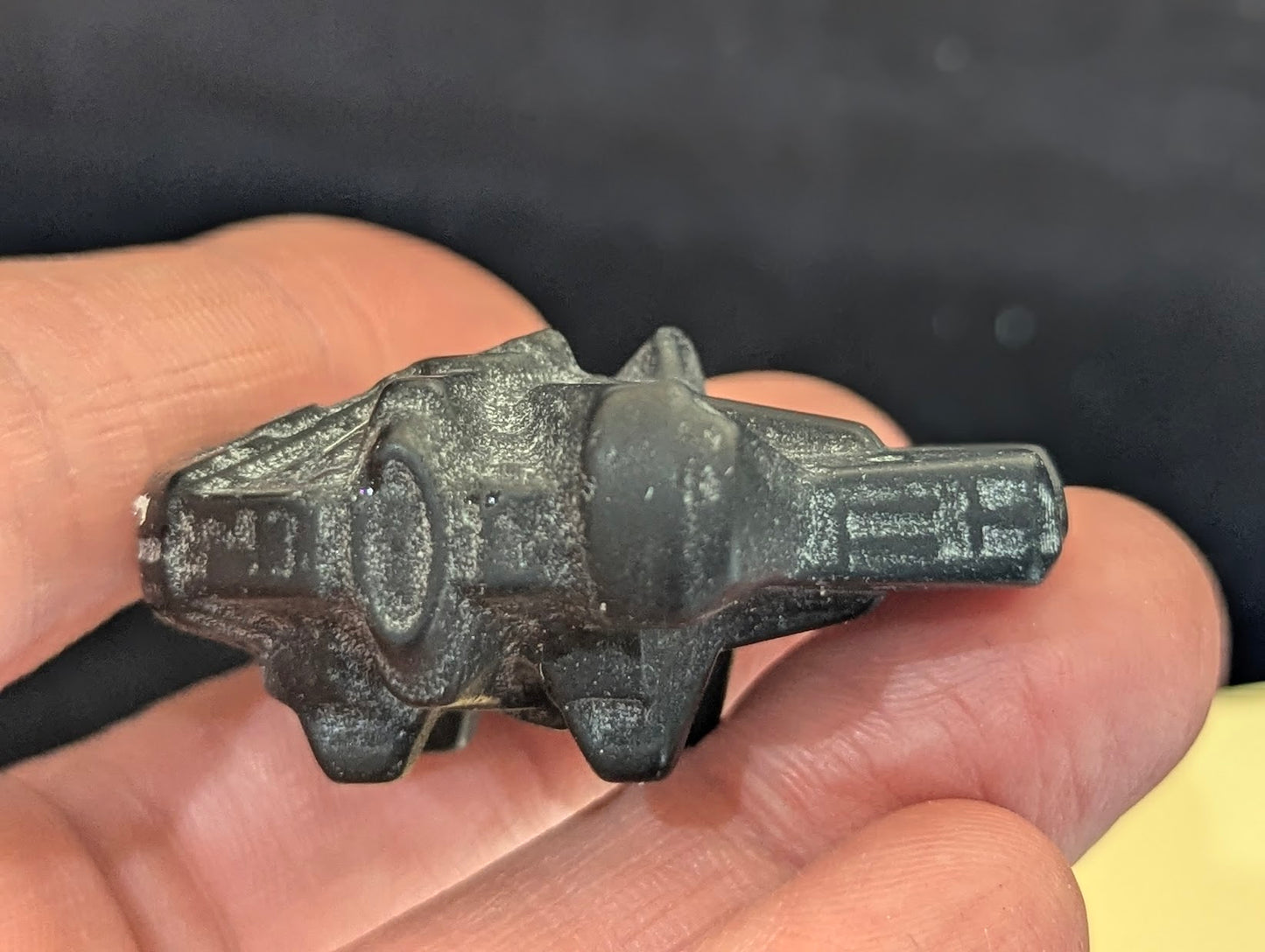 Profile view of a matte black obsidian Millennium Falcon carving held between fingers to show thickness and scale.