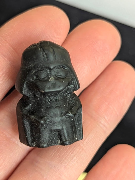 Front view of a matte black obsidian Darth Vader carving held in hand, showing textured volcanic glass and recessed details.