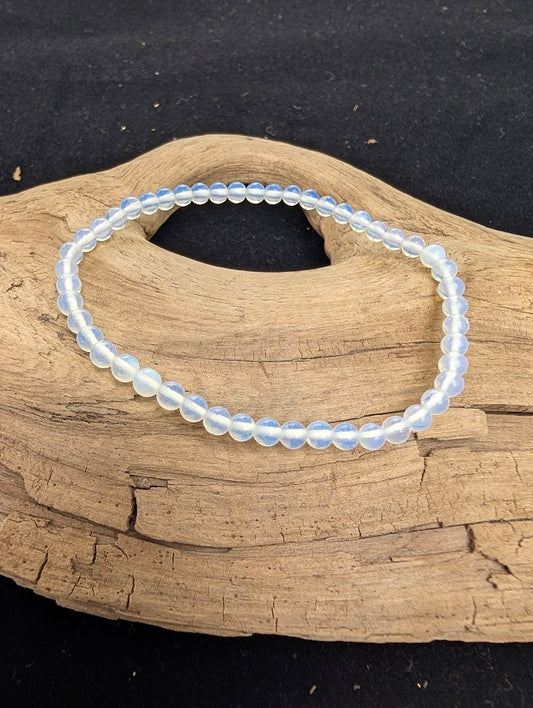 4mm polished Opalite beaded stretch bracelet resting on a driftwood display, showing milky blue and translucent opalescent tones.