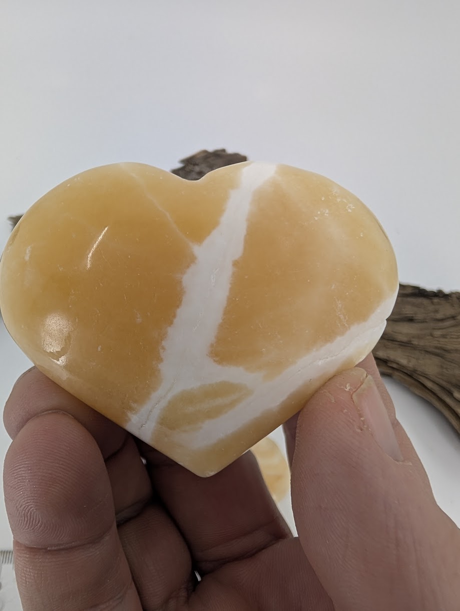Hand holding a medium 115g Orange Calcite heart showing white banding.