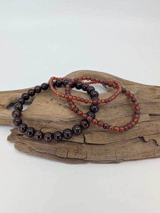 Three peach garnet bracelets in 3mm, 4mm, and 7mm stacked on driftwood