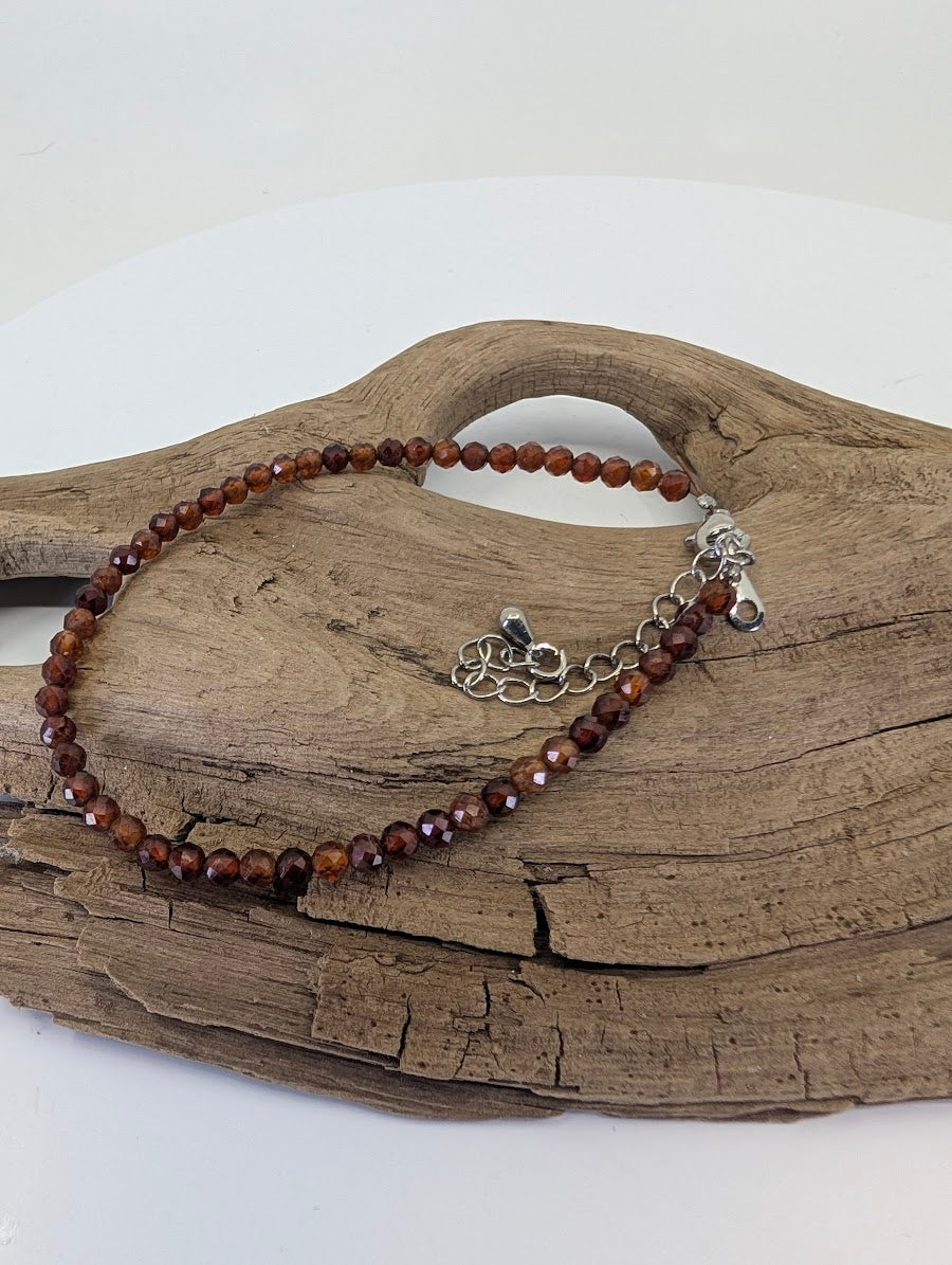 Dainty 3mm faceted Peach Garnet bracelet from Tanzania displayed on natural wood showing apricot tones.