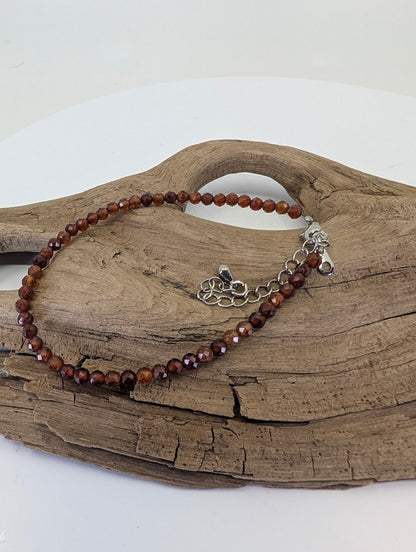 Dainty 3mm faceted Peach Garnet bracelet from Tanzania displayed on natural wood showing apricot tones.