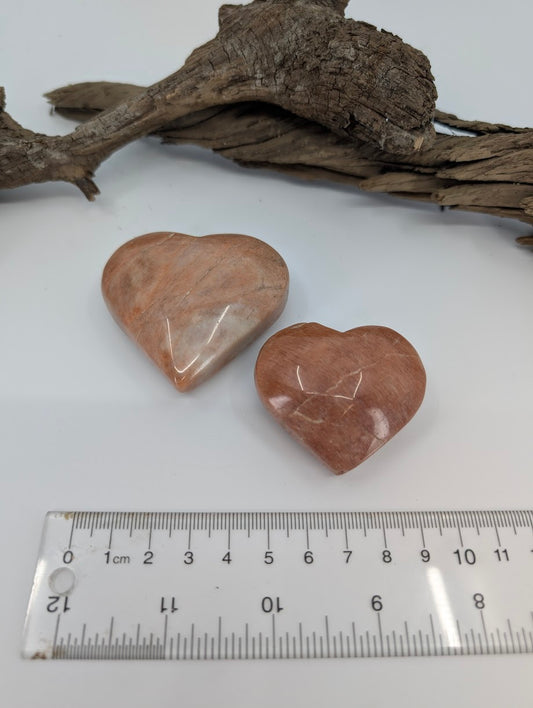 Pair of Peach Moonstone hearts showing warm tan and apricot colors on driftwood.