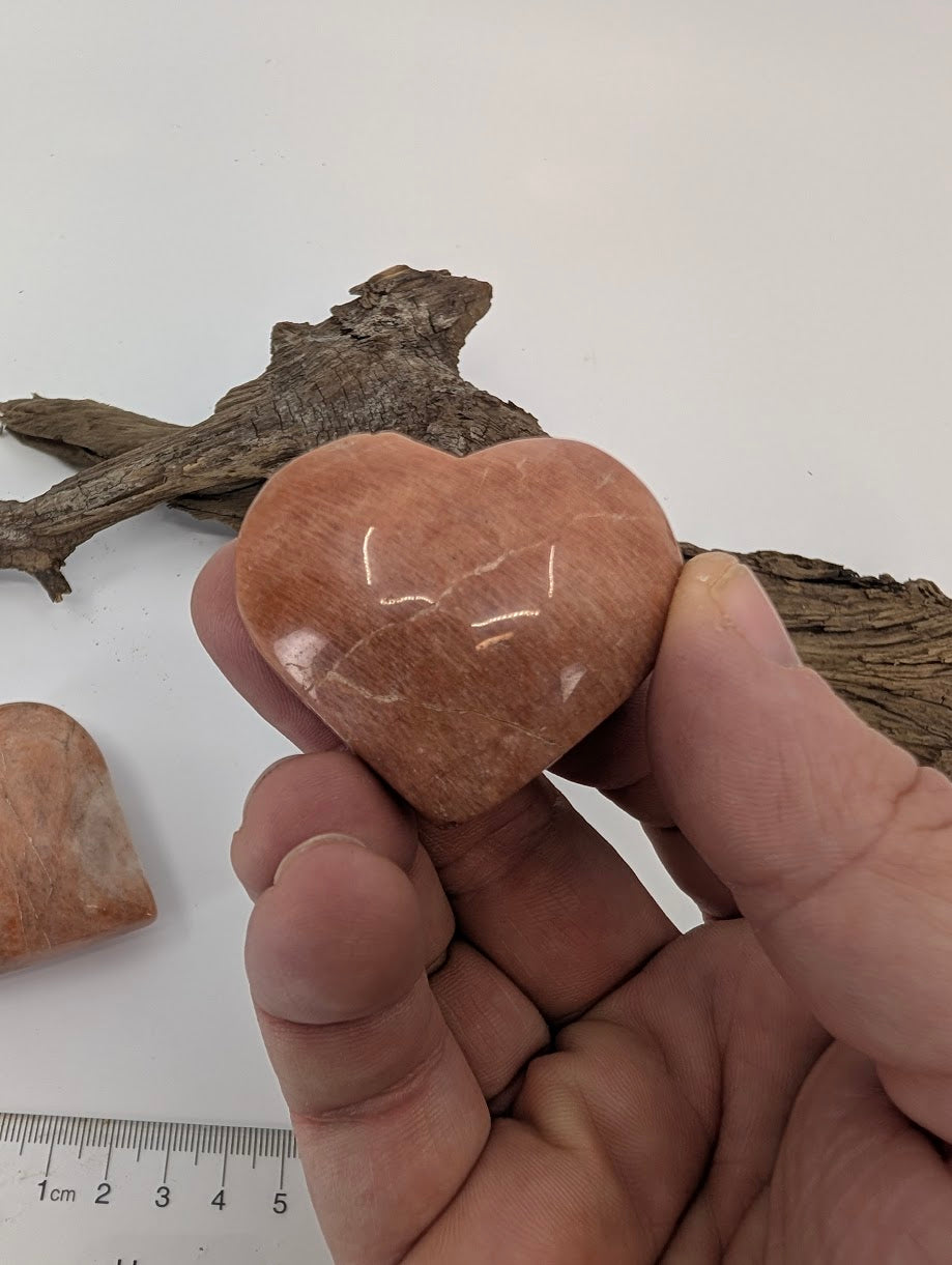 Hand holding a medium 70g Peach Moonstone heart showing sheen and polish.