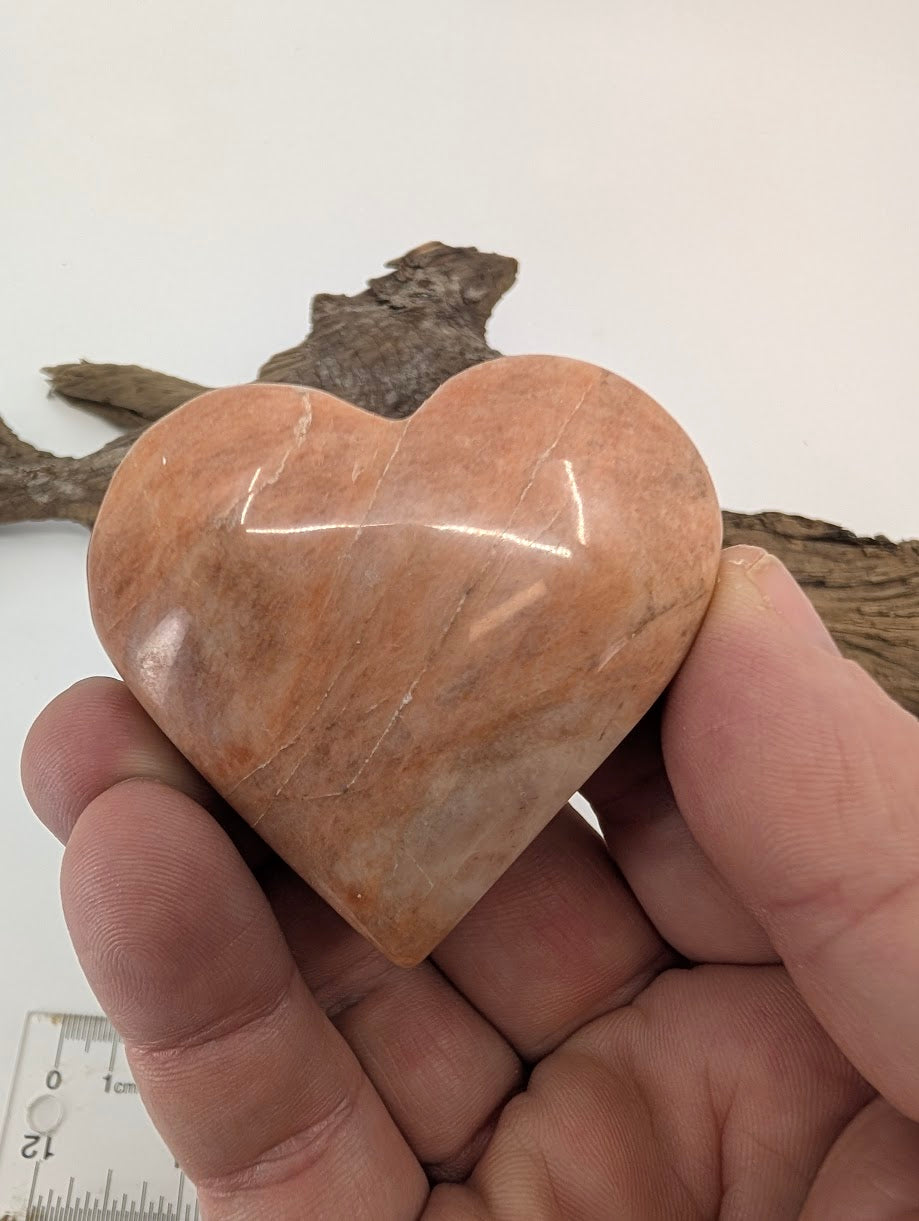 Hand holding a medium 85g Peach Moonstone heart showing sheen and polish.