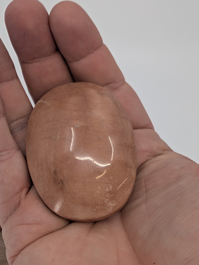 Peach Moonstone palm stone in hand showing polished finish, peach hue, and light reflection