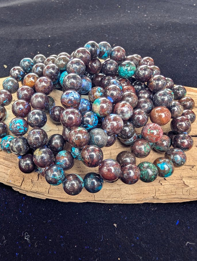 A stacked pile of multiple 8mm polished Phoenix Stone beaded stretch bracelets showing varied copper and teal patterns.